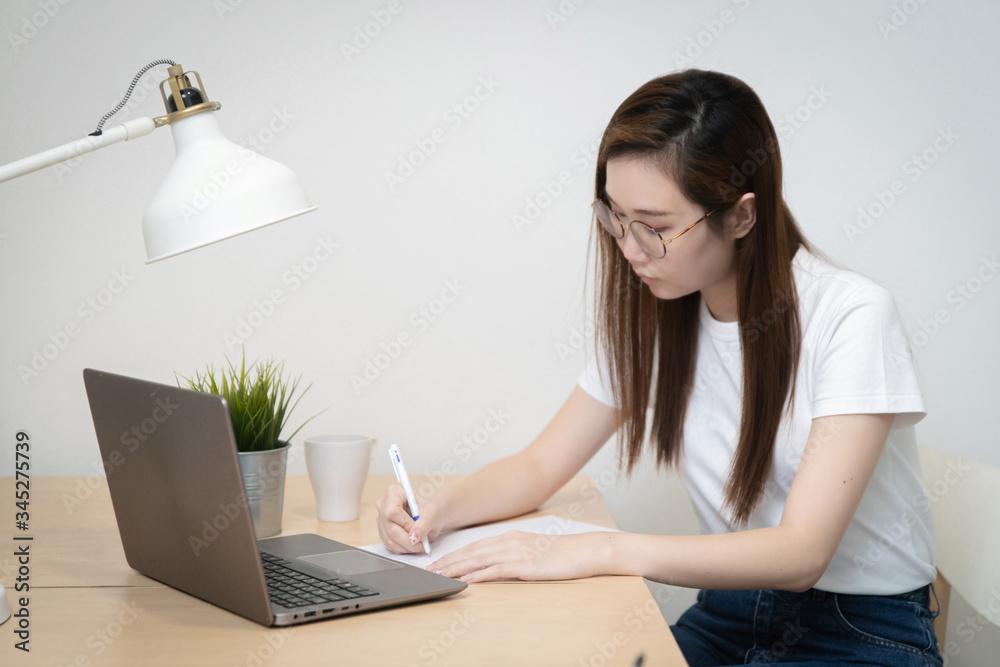 Fototapeta premium Asian woman wear white T-Shirt is working from home during coronavirus or COVID-19 with laptops and computers, quarantine for coronavirus