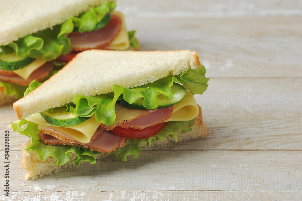 Obraz premium Sandwich with ham and cheese made of white bread. Light wooden background. Free space for text.