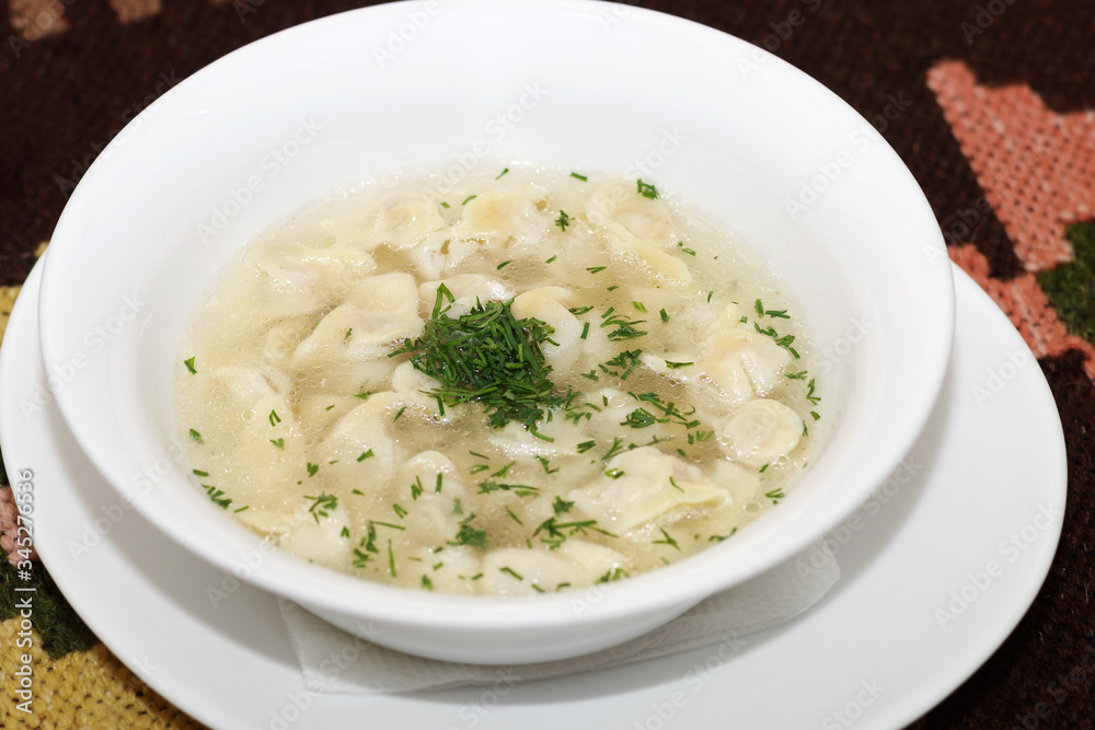 Soup with dumplings in a white plate.  Chuchvara, dyushbara- a dish of Central Asian, Caucasian, Tatar, Russian cuisines.
