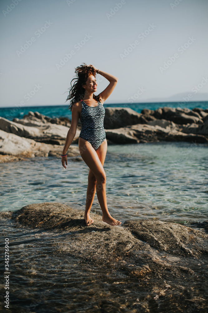 Young woman in bikini walking on rocks by the sea