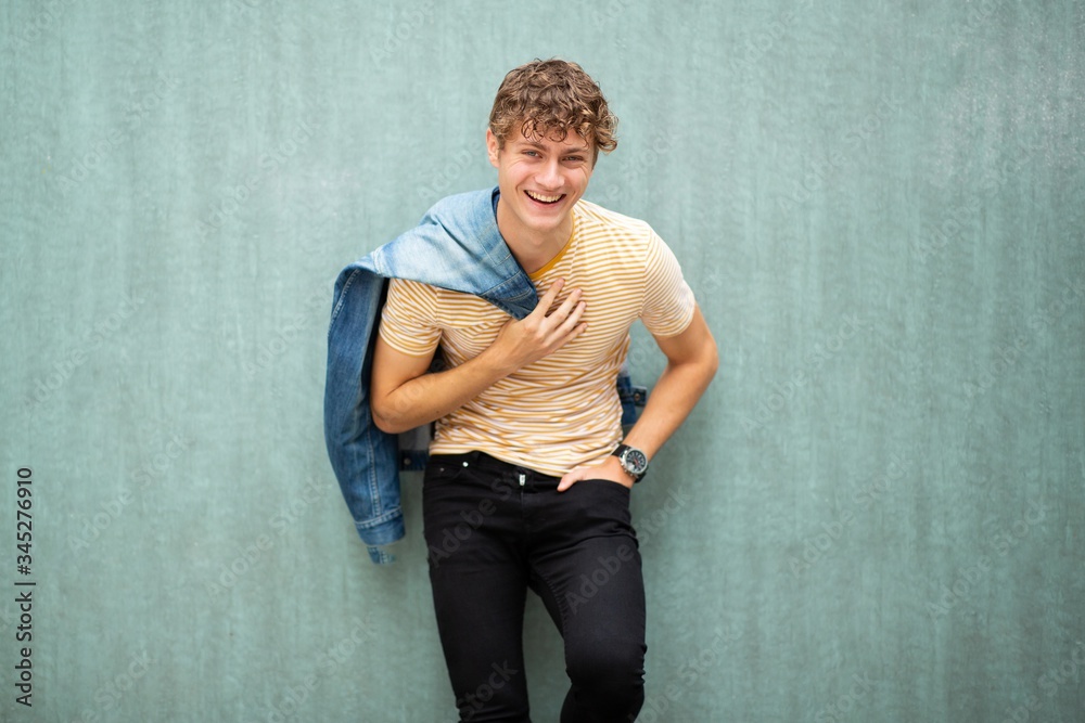 laughing man posing by green wall with denim jacket over shoulder laughing man posing by green wall with denim jacket over shoulder