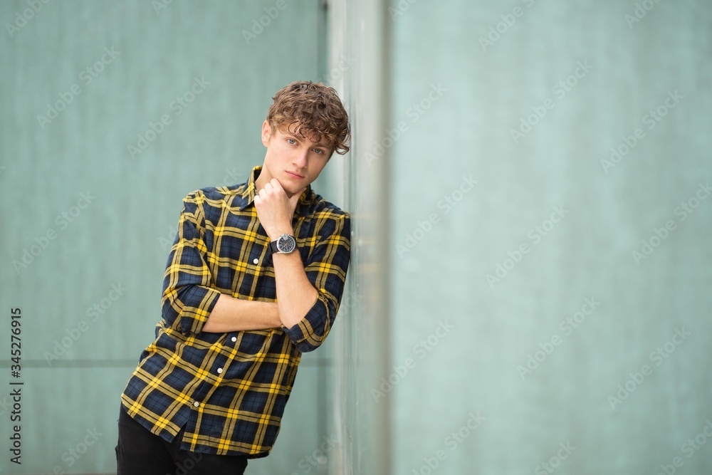 handsome young man with arms crossed leaning by green wall