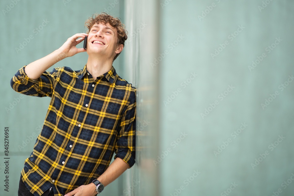 happy young man leaning against green wall talking with phone happy young man leaning against green wall talking with phone