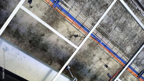 Cable tray with wires and metal duct show above t-bar grid in opened suspended (drop) ceiling and below concreate of upper floor at construction site of industrial building photo