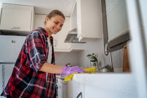 Young charming happy smiling girl woman rubs surface in the kitchen. House Hygiene and Cleaning Service Concept