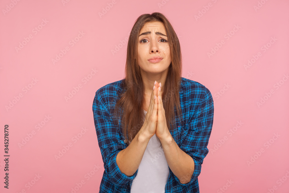 Please! Portrait of girl in checkered shirt holding hands in prayer, looking with imploring pleading expression, begging help, asking forgiveness. indoor studio shot isolated on pink background Please! Portrait of girl in checkered shirt holding hands in prayer, looking with imploring pleading expression, begging help, asking forgiveness. indoor studio shot isolated on pink background