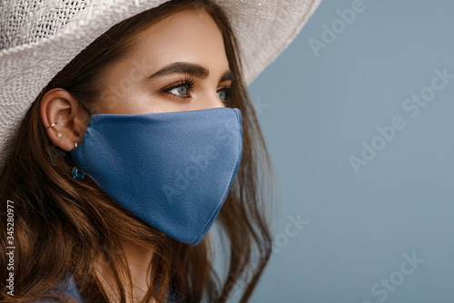 Woman wearing stylish protective face mask, posing on blue background. Trendy Fashion accessory during quarantine of coronavirus pandemic. Close up studio portrait. Copy, empty space for text