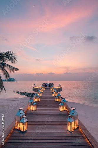 Fototapeta Naklejka Na Ścianę i Meble -  Romantic dinner on the beach with sunset, candles with palm leaves and sunset sky and sea. Amazing view, honeymoon or anniversary dinner landscape. Exotic island evening horizon, romance for a couple 