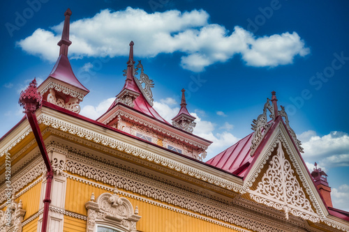 Yellow wooden house with carved patterns on a background of a beautiful blue sky with white clouds. Tomsk wooden architecture.