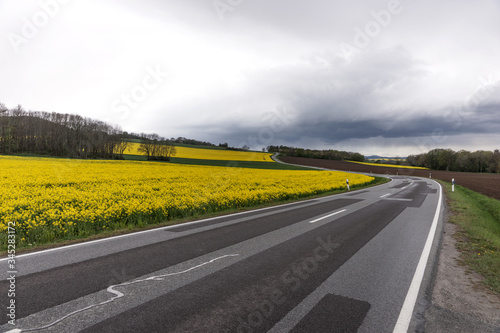Flowering rapeseed field next to a winding road in the mountains with dramatic clouds in the background