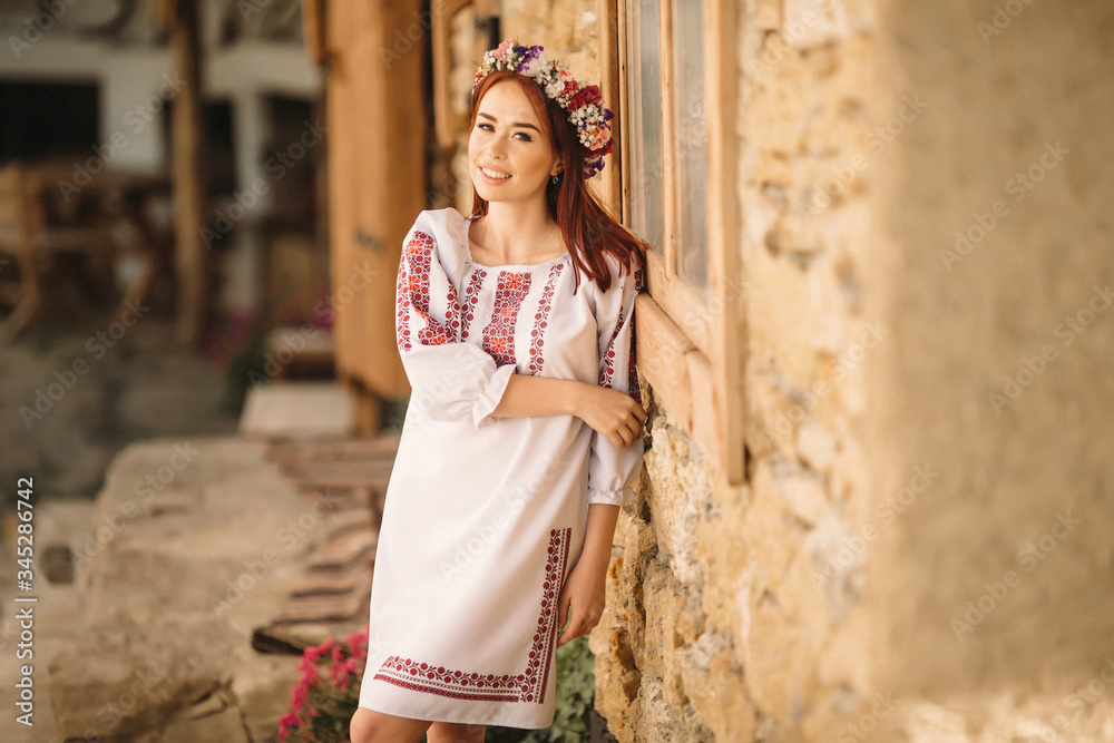 Young redhead moldavian girl dressed in traditional costume standing against a stone wall. Young redhead moldavian girl dressed in traditional costume standing against a stone wall.