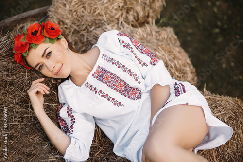 Schilderij op canvas Young  redhead moldavian girl dressed in traditional costume rests on the hay on