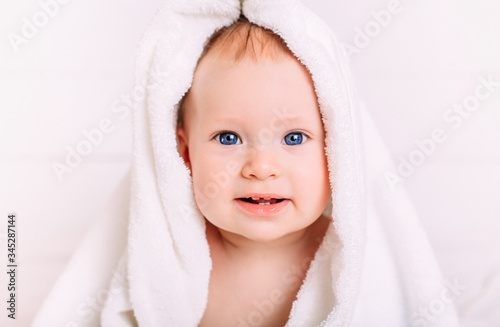 A cute baby with blue eyes wrapped in a white towel as the hood looks into the camera.