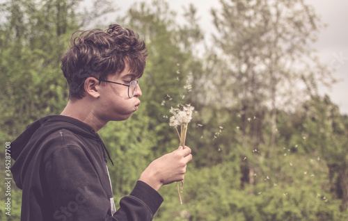 Kid blowing dandelions seeds in the wind in the countryside. A young man in nature, spring. Memories of youth, childhood