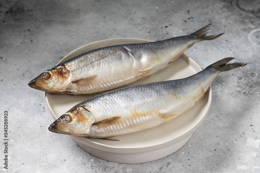 Herring on a white plate on a light gray table. Salted fish