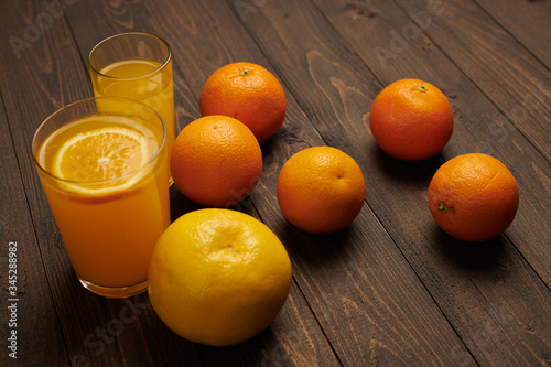 Fresh orange fruits whole and sliced on a dark wooden background - natural and healthy food. Glass of fruit cocktail.