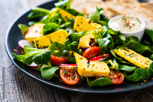 Fresh salad - blue cheese, cherry tomatoes, vegetables and homemade bread on wooden background 