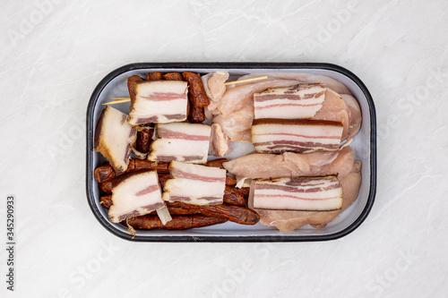 Top view of mixed meat prepared for grill. Bacon kebabs sausages and chicken breasts.