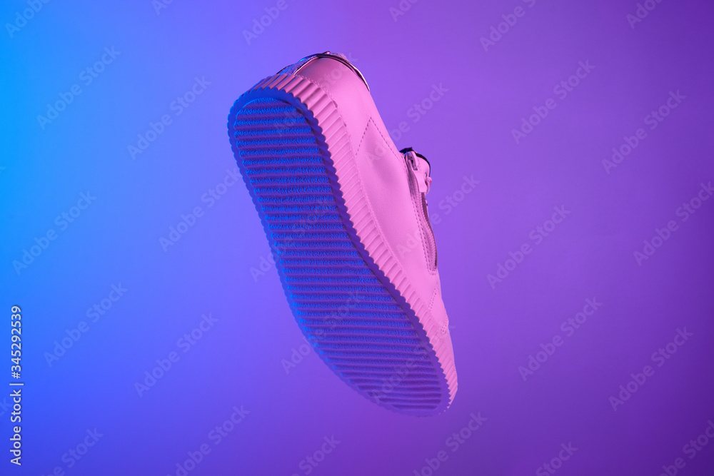 Trendy white teenage sneaker flying in trendy neon light. Levitation Shoe in red, blue light. Creative minimalism. Trendy white teenage sneaker flying in trendy neon light. Levitation Shoe in red, blue light. Creative minimalism.