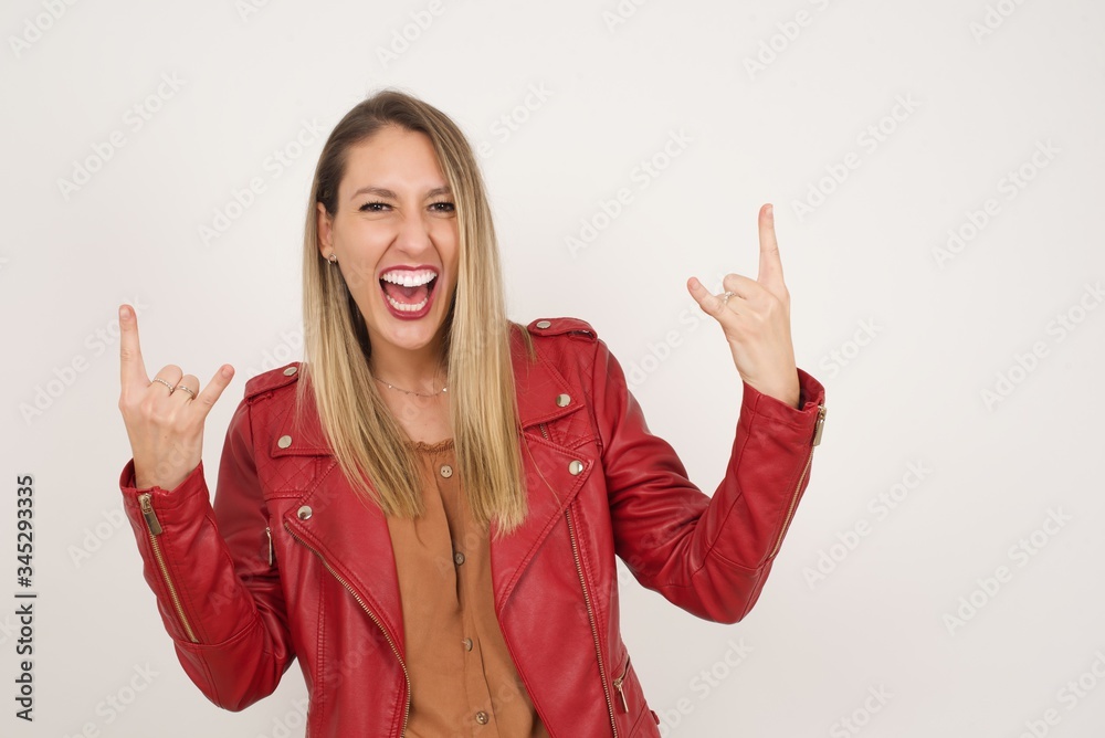 Born to rock this world. Joyful woman in fashionable clothes screaming out loud and showing with raised arms horns or rock gesture, expressing excitement of being on concert of band. Born to rock this world. Joyful woman in fashionable clothes screaming out loud and showing with raised arms horns or rock gesture, expressing excitement of being on concert of band.