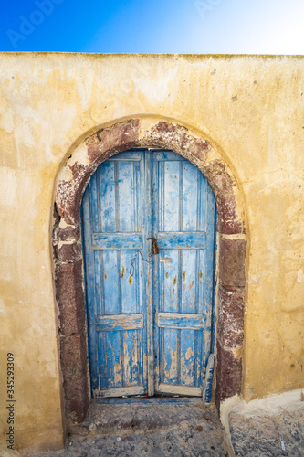old blue wooden door and yellow wall in Oia street, Architecture, picturesque, Santorini island, Cyclades, Greece
