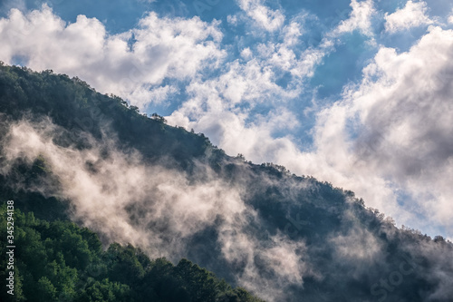 High mountains with green slopes and rocks hidden in thick clouds and fog.