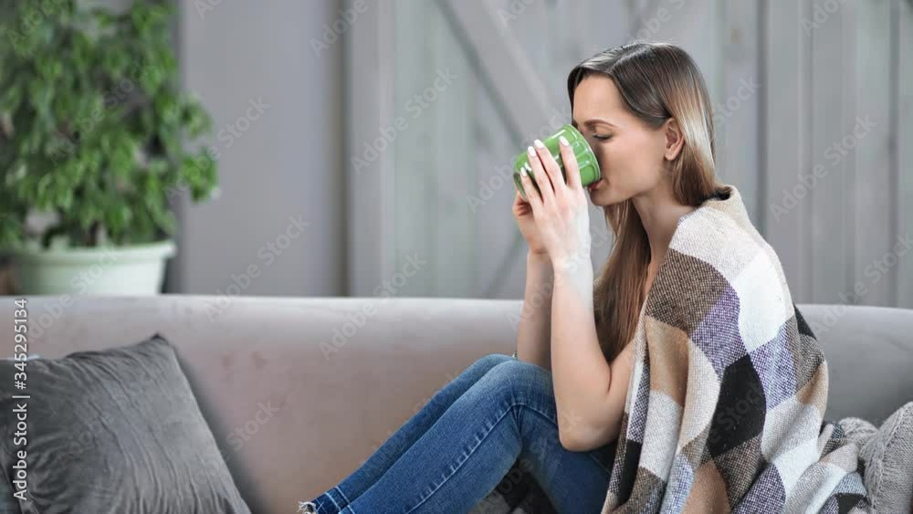 Smiling relaxed young woman drinking hot beverage sitting on couch. Shot with RED camera in 4K Smiling relaxed young woman drinking hot beverage sitting on couch. Shot with RED camera in 4K