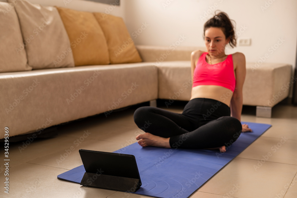 A young girl goes in for sports at home on a blue mat, dressed in sportswear. Online classes on the tablet. Yoga, healthy lifestyle. Sports during viruses and self-isolation at home. Horizontal view. A young girl goes in for sports at home on a blue mat, dressed in sportswear. Online classes on the tablet. Yoga, healthy lifestyle. Sports during viruses and self-isolation at home. Horizontal view.