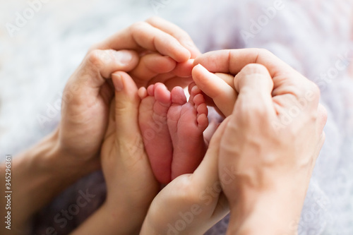 Legs of a newborn in the hands of parents on a white background. Little legs of a newborn baby in a big hand of an adult. Newborn baby feet in the hands of the mother on a light background blanket.