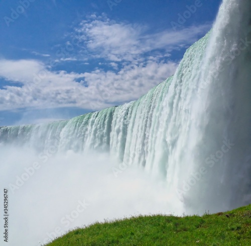 A view of Niagara falls from Canadian site with green grass and blue sky with little bit of clouds