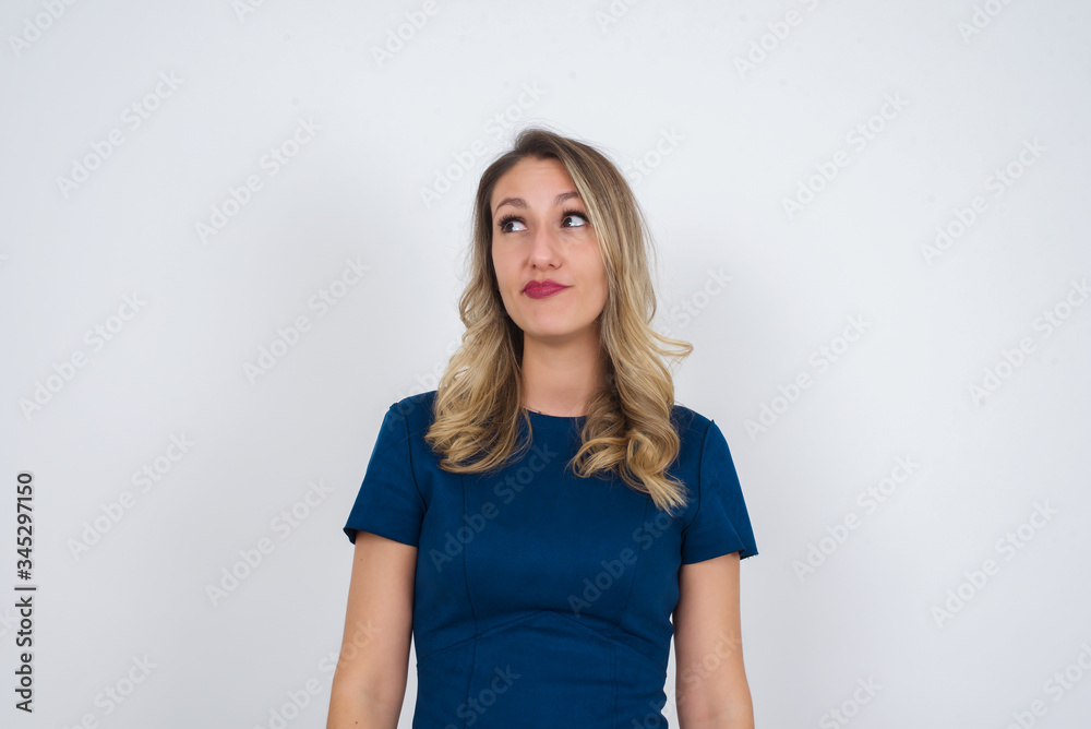 Troublesome puzzled Caucasian woman frowns face, bites lip, raises eyebrows, looks up, has problems, dressed in fashionable clothes, isolated over gray background, has regret look. Troublesome puzzled Caucasian woman frowns face, bites lip, raises eyebrows, looks up, has problems, dressed in fashionable clothes, isolated over gray background, has regret look.