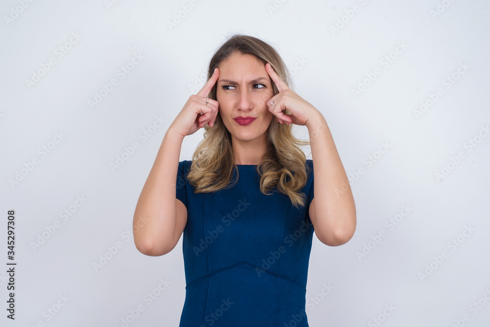 Dreamy Caucasian female with thoughtful expression, looks away, keeps hand near face, thinks about something pleasant, poses against gray wall. Dreamy Caucasian female with thoughtful expression, looks away, keeps hand near face, thinks about something pleasant, poses against gray wall.