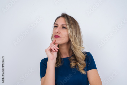 Portrait of thoughtful  woman keeps hand under chin, looks away trying to remember something or listens something with interest, dressed casually, poses indoors. Youth concept.
