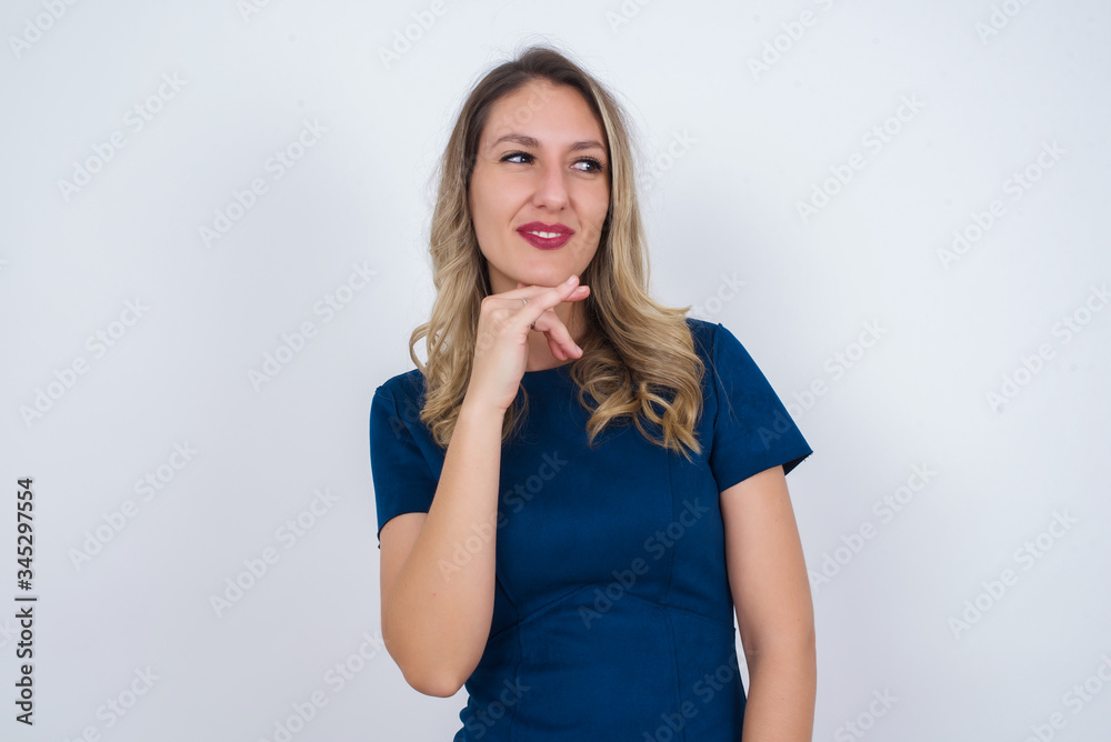 Dreamy female with pleasant expression, wearing casual clothes, looks sideways, keeps hand under chin, thinks about something pleasant, poses against gray background. Dreamy female with pleasant expression, wearing casual clothes, looks sideways, keeps hand under chin, thinks about something pleasant, poses against gray background.
