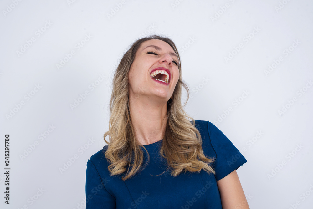 Joyful European woman having fun and laughs at good joke or sings wears casual clothes, standing against gray wall. Happy woman with long hair poses inddoors. Joyful European woman having fun and laughs at good joke or sings wears casual clothes, standing against gray wall. Happy woman with long hair poses inddoors.