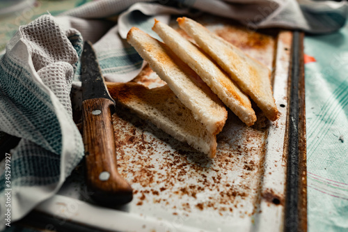 Triangular slices of toasted white bread with a soft texture inside and a crisp crust on the outside on a rusty metal background, next to an old knife with a wooden handle