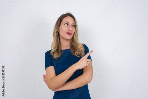 Pretty brunette woman posing on camera with tricky look and gesturing to side. Female designer presenting lovely product with index finger. Gesture concept.
