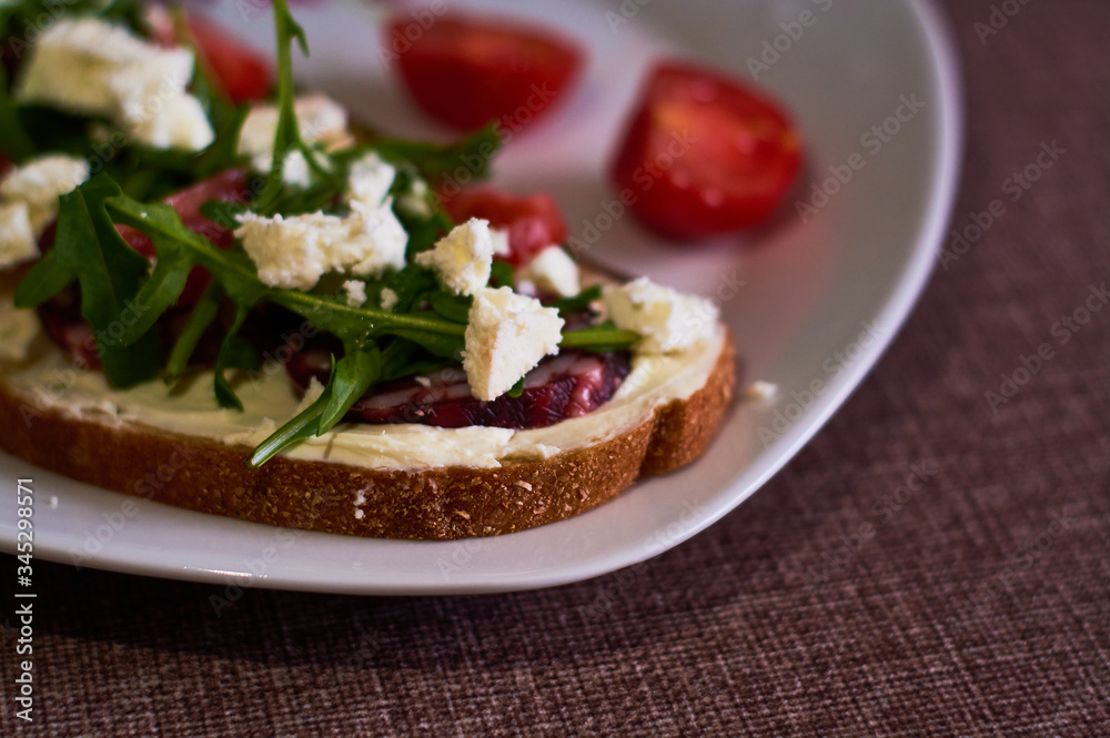 Large toast of rye bread with pieces of cheese, arugula, cherry tomatoes and sausage.