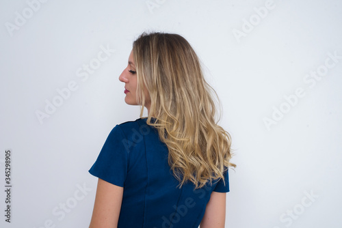 The back side view of a girl with long straight wavy and shiny hair standing against gray wall. Studio Shoot.ï¿½