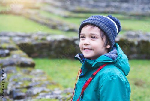 Portrait of School kid explore and learning about history with school trip  Happy child boy wearing hat and winter cloths standing alone with blurry ruins of old abbey background
