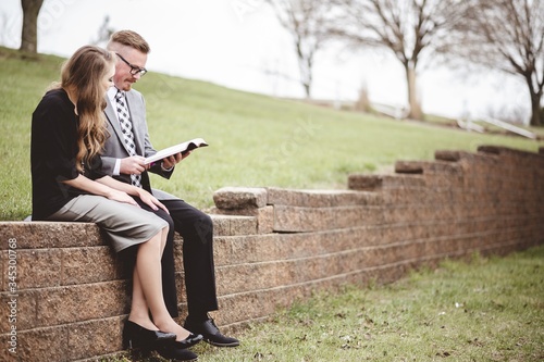 View of a couple wearing formal clothes while reading a book together in a garden photo