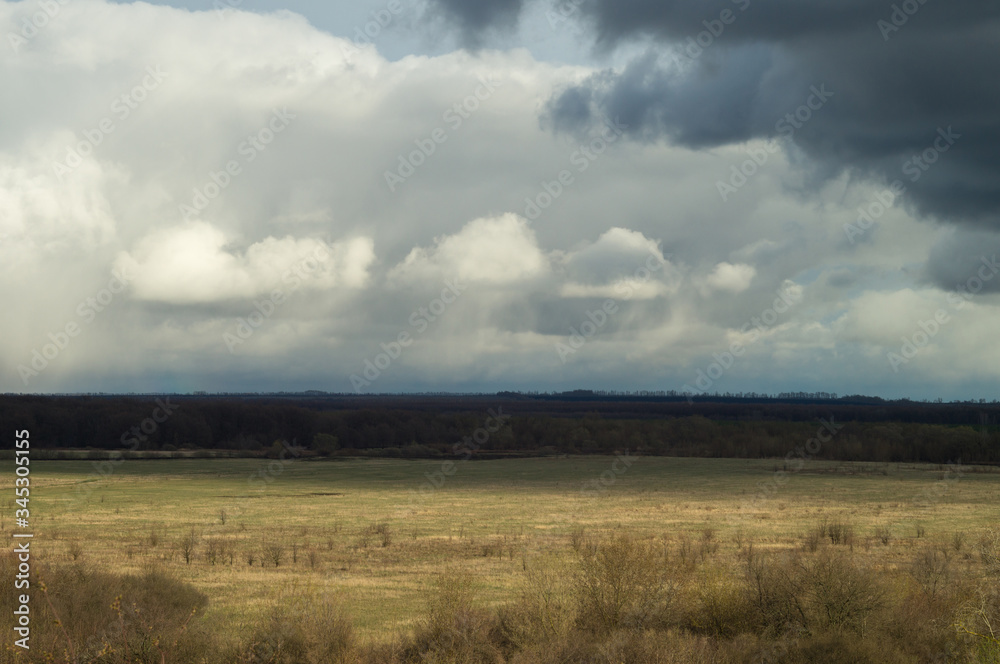 Air view from the hill to spring pasture valley under a moody cloudy sky. Landscape of remote places yellow blue motive