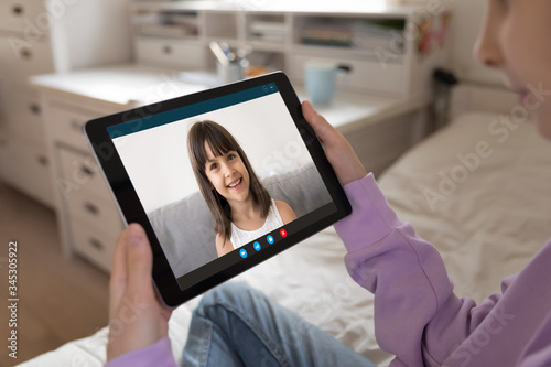 Close up of young girl talk chat on video call on tablet with smiling little girlfriend, quarantine at home, teen child have online webcam conversation with sister or friend, use modern pad device