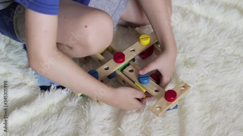 A little boy collects a plane from a wooden designer on a fluffy bedspread. Children's educational games