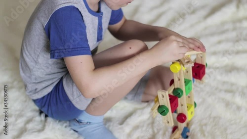 A little boy collects a plane from a wooden designer on a fluffy bedspread. Children's educational games