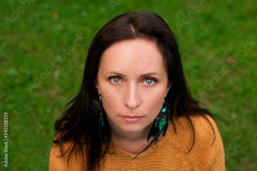 Close-up portrait of a woman with dark hair and blue eyes against a background of green grass