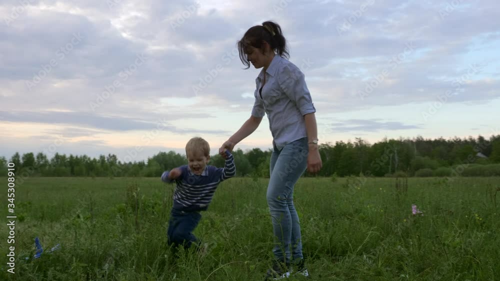 Happy Joyful Child Running Around Mother. Playing in the Field on Nature. Evening Twilight Rural Scene Happy Joyful Child Running Around Mother. Playing in the Field on Nature. Evening Twilight Rural Scene