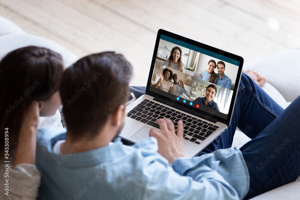 Back view of young couple relax on couch speak talk on video call with multiracial friends, man and woman spouses rest on sofa at home engaged in webcam conference conversation with relatives Back view of young couple relax on couch speak talk on video call with multiracial friends, man and woman spouses rest on sofa at home engaged in webcam conference conversation with relatives