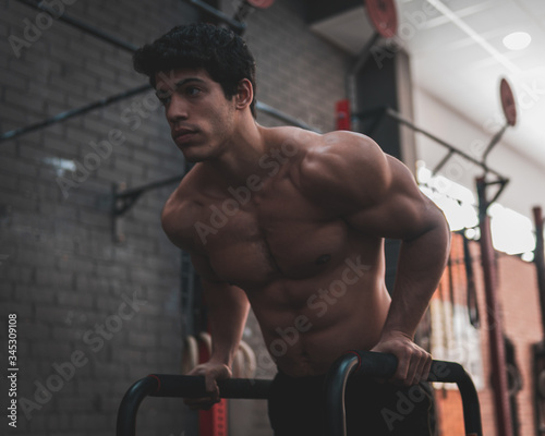 Obraz na plátně Young, shirtless, muscular athlete doing some dips in parallel bars in the gym