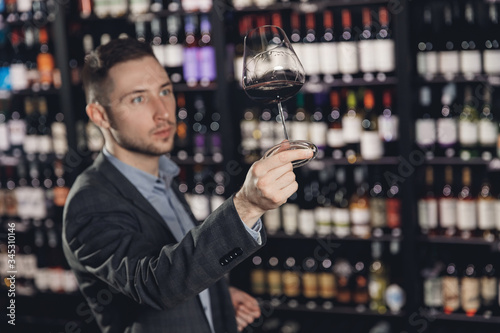Man sommelier is holding glass of wine and tasting transparency light sediments in restaurant